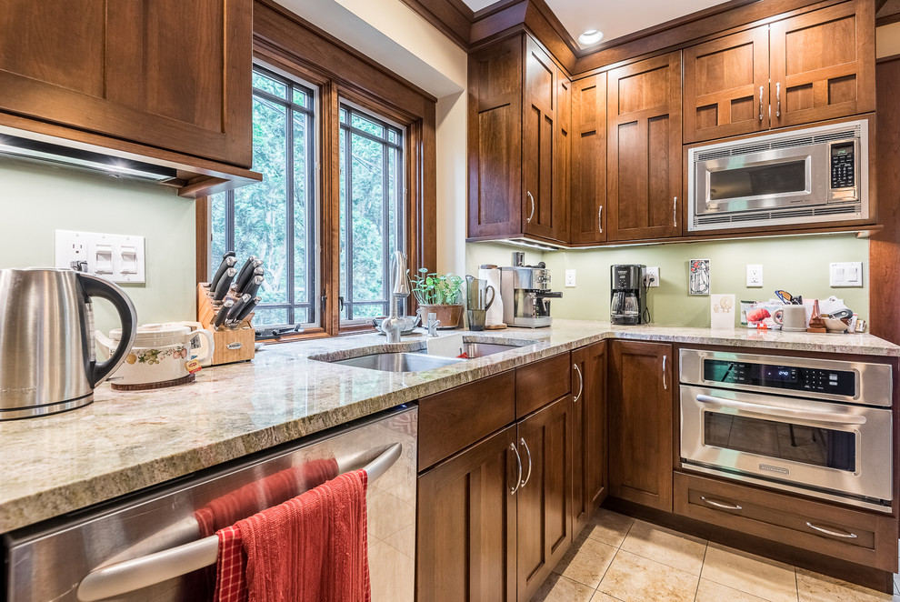 Large arts and crafts u-shaped eat-in kitchen in Chicago with a double-bowl sink, shaker cabinets, medium wood cabinets, granite benchtops, green splashback, stainless steel appliances, ceramic floors and multiple islands.