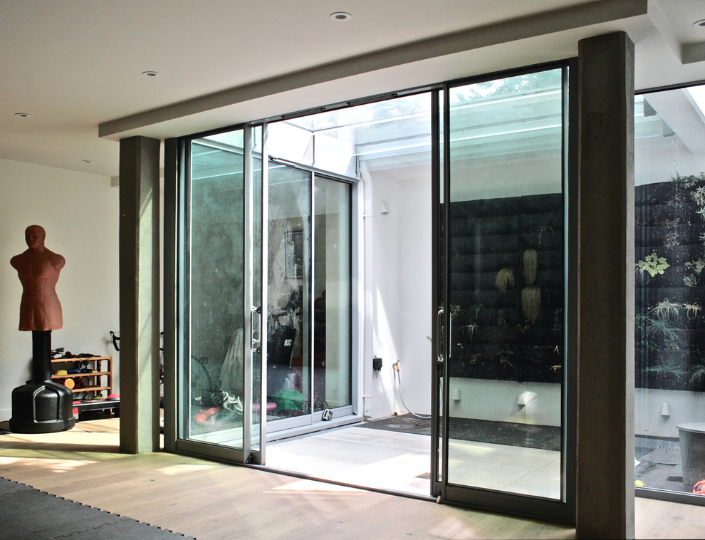 Large contemporary fully buried basement in London with white walls, light hardwood floors and beige floor.
