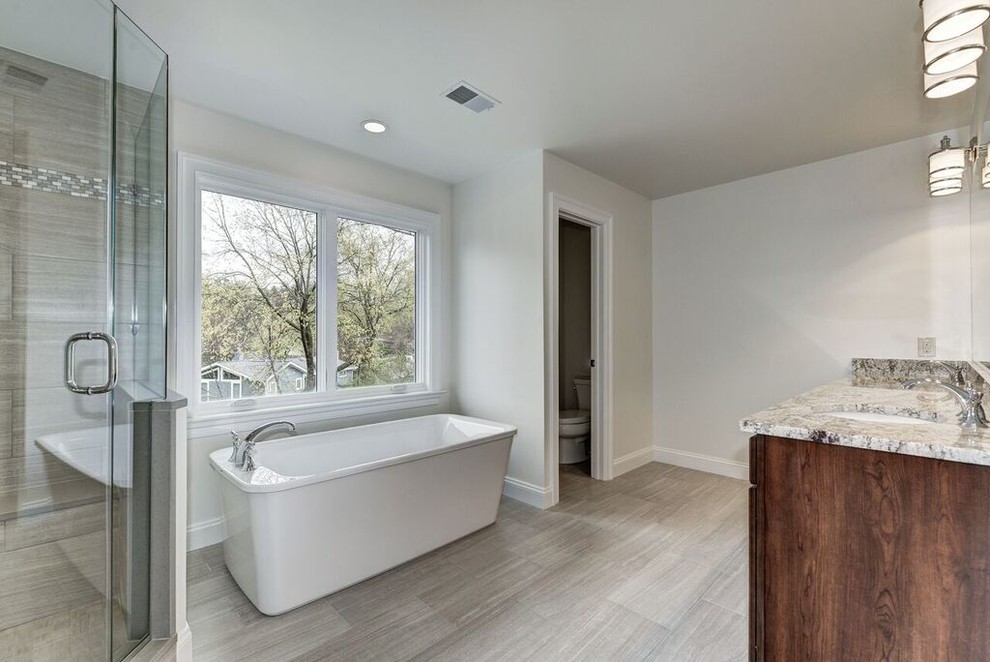 Large transitional master gray tile and stone tile ceramic tile freestanding bathtub photo in DC Metro with beaded inset cabinets, medium tone wood cabinets, a one-piece toilet, white walls, a drop-in sink and marble countertops