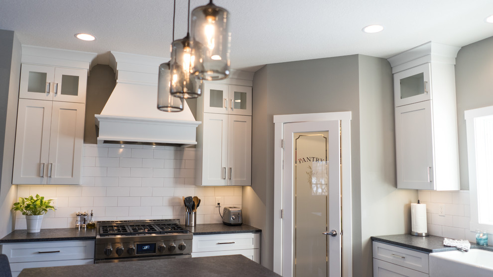 Large transitional u-shaped eat-in kitchen photo with a farmhouse sink, flat-panel cabinets, white cabinets, granite countertops, white backsplash, ceramic backsplash, stainless steel appliances and an island