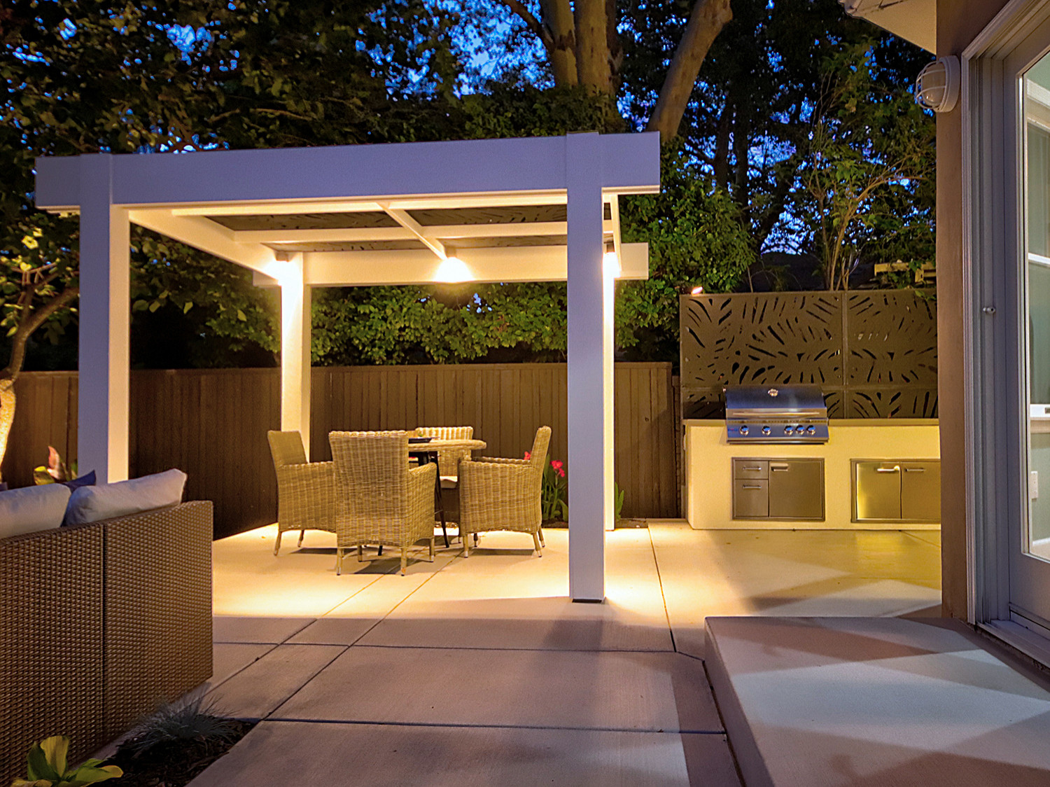 Evening Ambiance: Illuminated Pergola, Outdoor Kitchen, and Seating Area