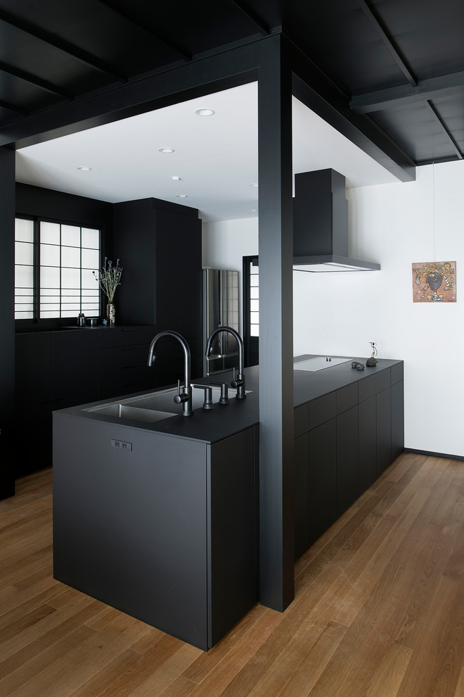 Inspiration for an asian single-wall open plan kitchen in Other with an undermount sink, beaded inset cabinets, black cabinets, black appliances, medium hardwood floors, a peninsula, brown floor and black benchtop.