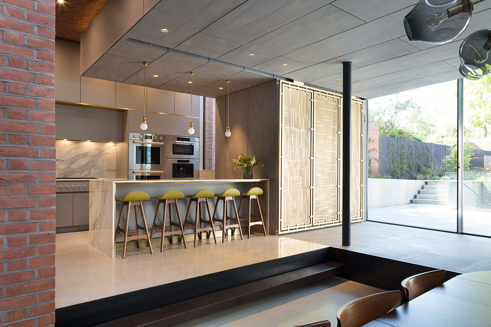 Large contemporary l-shaped open plan kitchen in London with a submerged sink, flat-panel cabinets, grey cabinets, marble worktops, white splashback, marble splashback, stainless steel appliances, concrete flooring, an island, grey floors and white worktops.