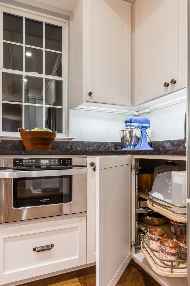 Mid-sized transitional l-shaped medium tone wood floor eat-in kitchen photo in Austin with an undermount sink, shaker cabinets, white cabinets, granite countertops, white backsplash, ceramic backsplash, stainless steel appliances and an island