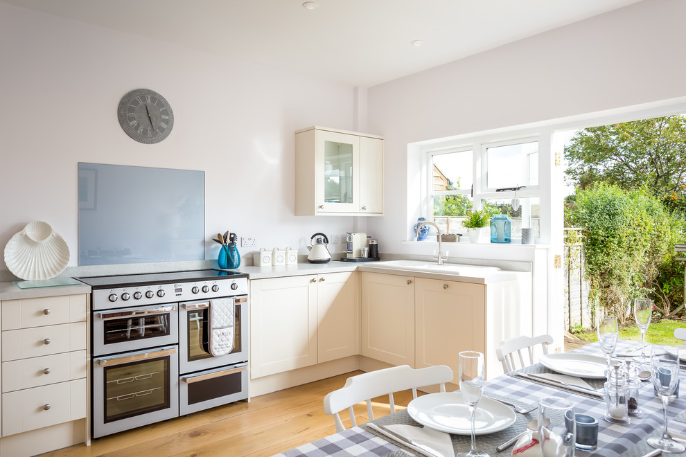 Photo of a mid-sized l-shaped eat-in kitchen in Gloucestershire with a drop-in sink, shaker cabinets, beige cabinets, quartz benchtops, blue splashback, glass tile splashback, stainless steel appliances, medium hardwood floors and no island.