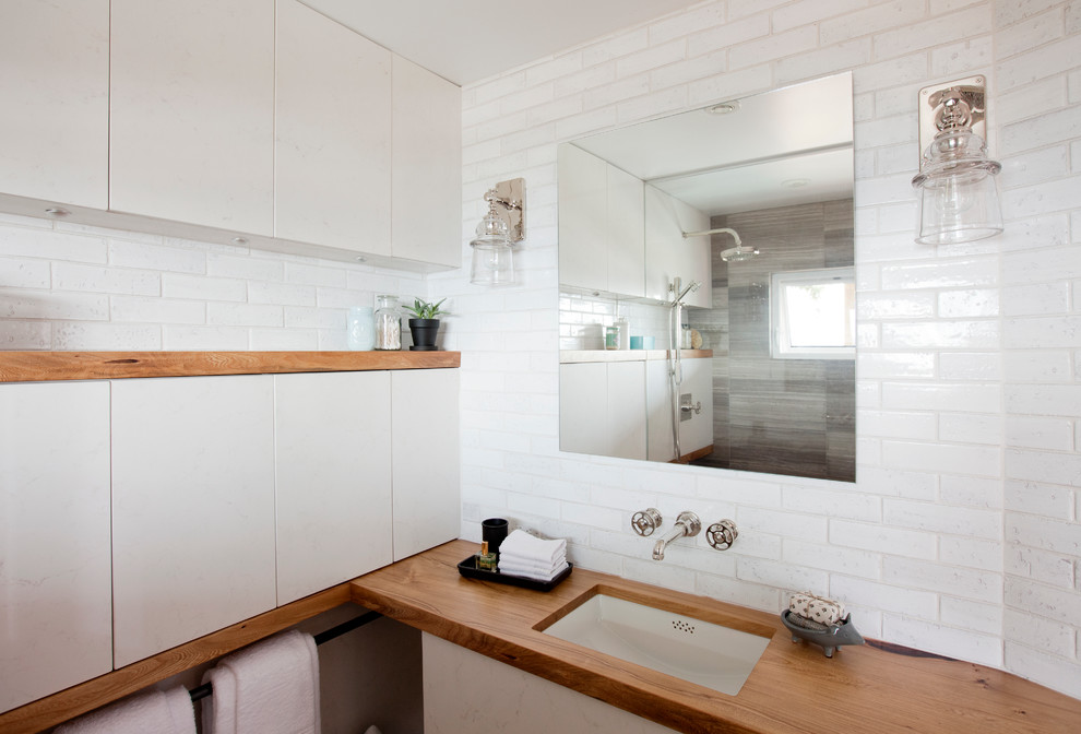 Photo of a small transitional master bathroom in Vancouver with flat-panel cabinets, white cabinets, an open shower, a two-piece toilet, white tile, stone slab, white walls, limestone floors, an undermount sink and wood benchtops.