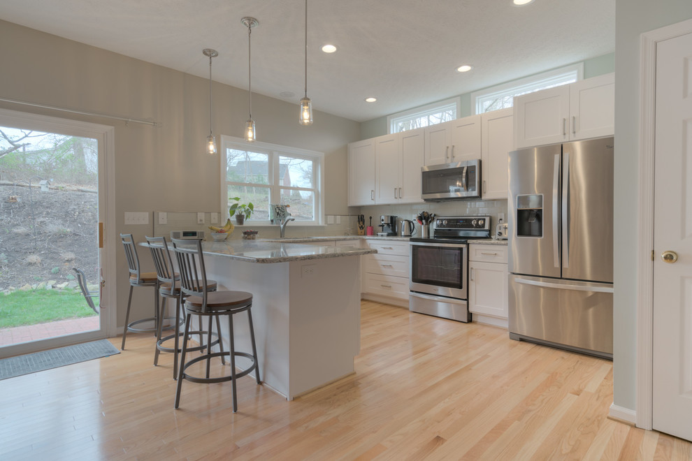 Inspiration for a mid-sized transitional u-shaped light wood floor eat-in kitchen remodel with an undermount sink, shaker cabinets, white cabinets, quartz countertops, beige backsplash, glass tile backsplash, stainless steel appliances and a peninsula
