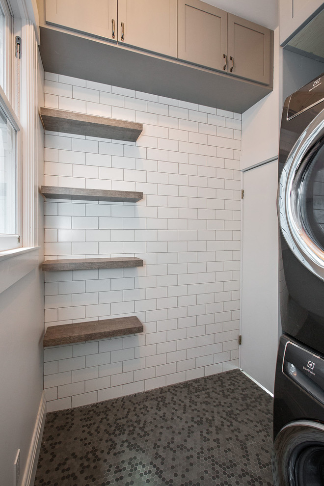 Photo of a small contemporary single-wall dedicated laundry room in San Francisco with recessed-panel cabinets, grey cabinets, white walls, porcelain floors, a stacked washer and dryer and grey floor.