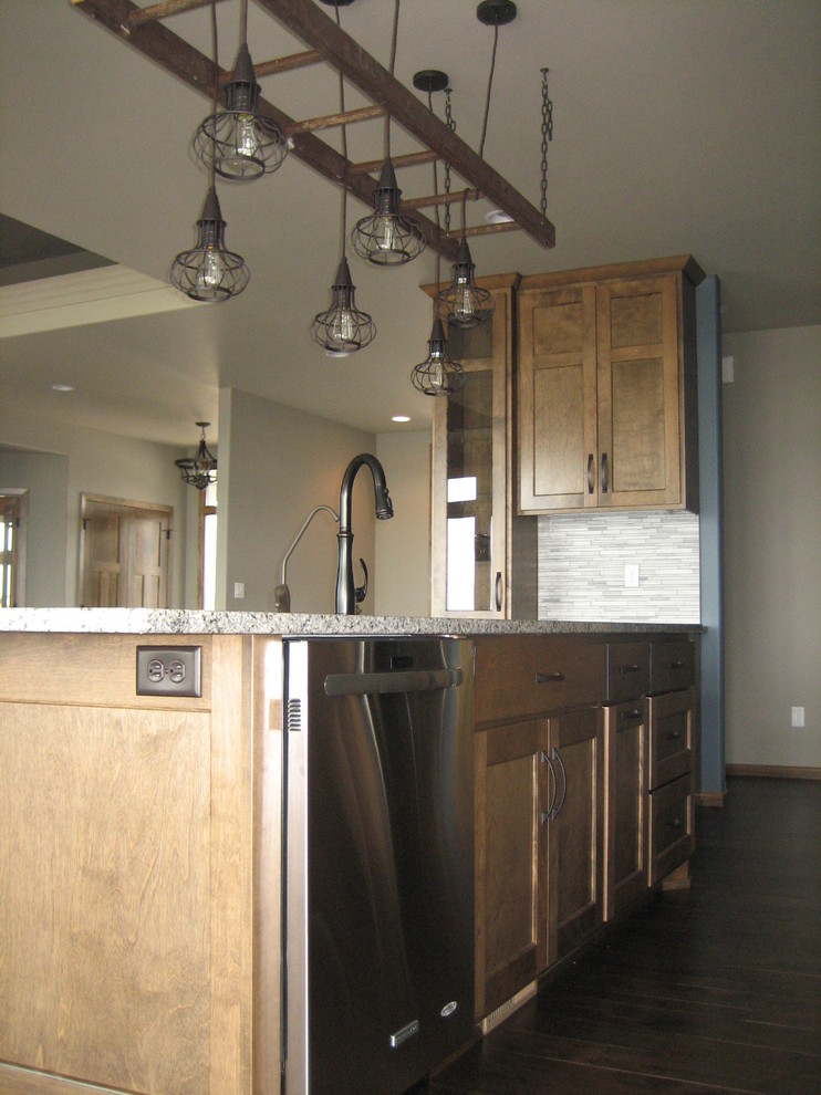 Mid-sized mountain style l-shaped dark wood floor open concept kitchen photo with an undermount sink, recessed-panel cabinets, medium tone wood cabinets, granite countertops, gray backsplash, glass tile backsplash, stainless steel appliances and an island