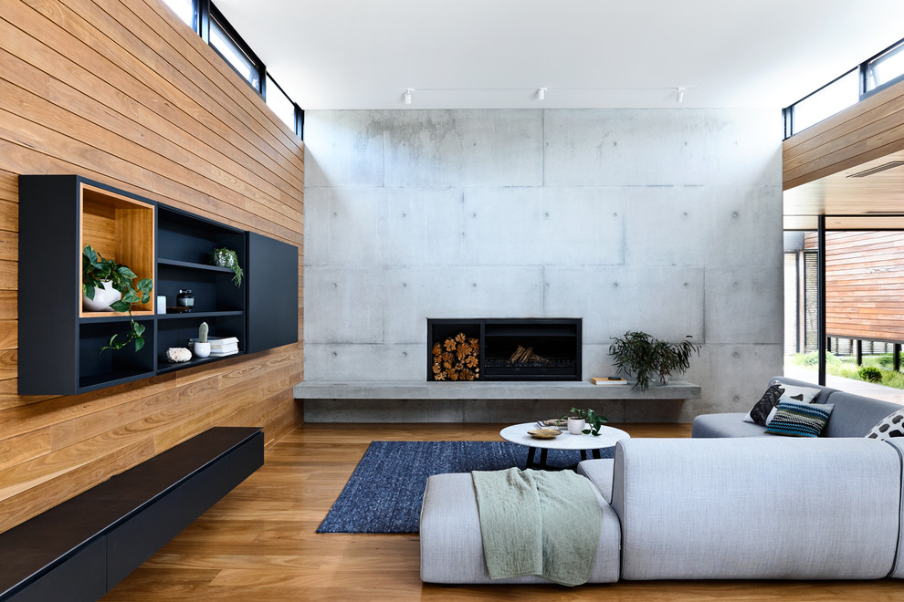 Photo of a contemporary formal open concept living room in Melbourne with medium hardwood floors, a standard fireplace, a concrete fireplace surround, grey walls and brown floor.