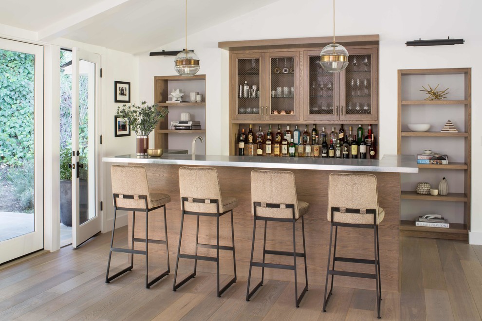 Photo of a mid-sized country galley seated home bar in Los Angeles with a drop-in sink, beaded inset cabinets, medium wood cabinets, zinc benchtops, grey benchtop and light hardwood floors.