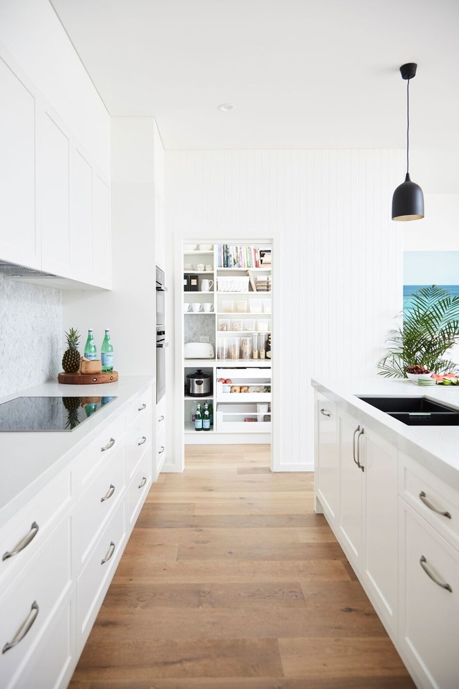 Design ideas for a contemporary galley kitchen pantry in Sydney with a drop-in sink, shaker cabinets, white cabinets, quartz benchtops, multi-coloured splashback, marble splashback, black appliances, light hardwood floors and multiple islands.