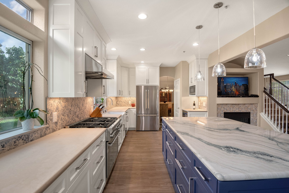 This is an example of a mid-sized mediterranean open plan kitchen in San Francisco with a farmhouse sink, shaker cabinets, white cabinets, quartzite benchtops, blue splashback, porcelain splashback, stainless steel appliances, porcelain floors, with island, grey floor and blue benchtop.