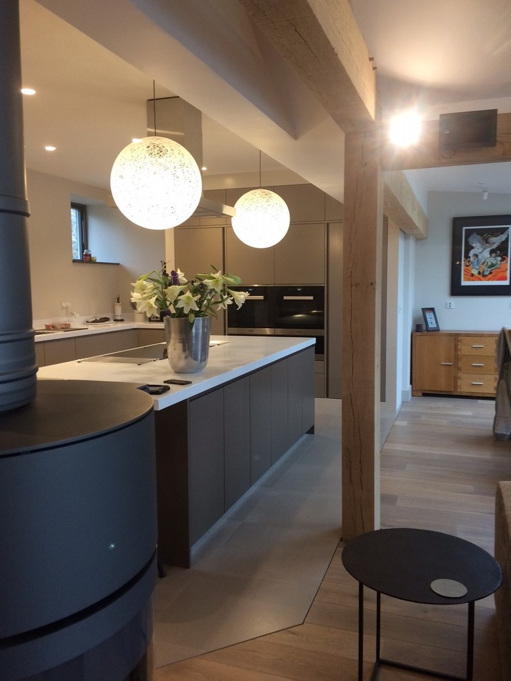 Photo of a mid-sized contemporary open plan kitchen in Devon with an integrated sink, flat-panel cabinets, brown cabinets, solid surface benchtops, stainless steel appliances, limestone floors and with island.