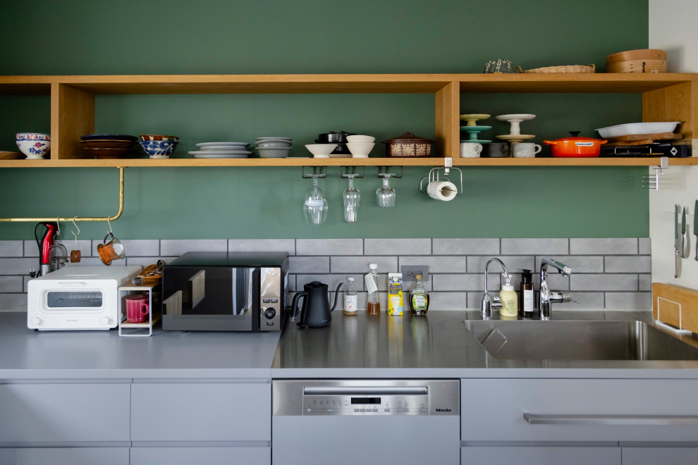 Rustik inredning av ett avskilt, mellanstort grå grått l-kök, med en undermonterad diskho, luckor med profilerade fronter, grå skåp, bänkskiva i rostfritt stål, grått stänkskydd, stänkskydd i porslinskakel, rostfria vitvaror, vinylgolv, flera köksöar och grått golv