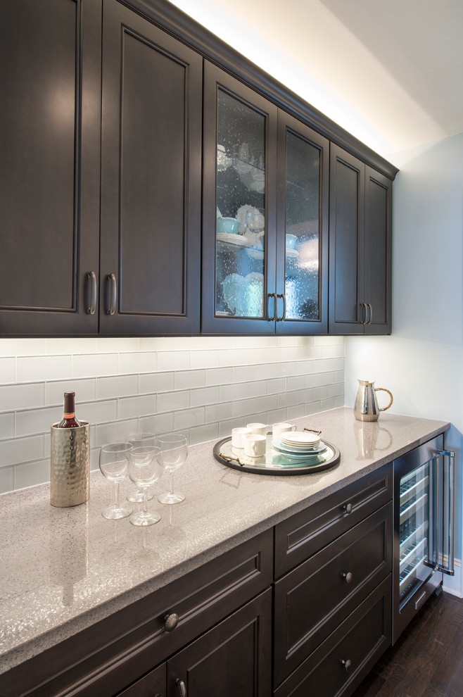 Design ideas for a mid-sized contemporary single-wall wet bar in Charleston with an undermount sink, raised-panel cabinets, dark wood cabinets, granite benchtops, grey splashback, glass tile splashback and light hardwood floors.