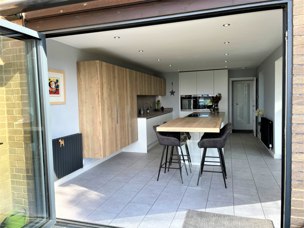 Photo of a medium sized contemporary l-shaped kitchen/diner in Other with a single-bowl sink, flat-panel cabinets, white cabinets, composite countertops, grey splashback, vinyl flooring, an island, grey floors and grey worktops.