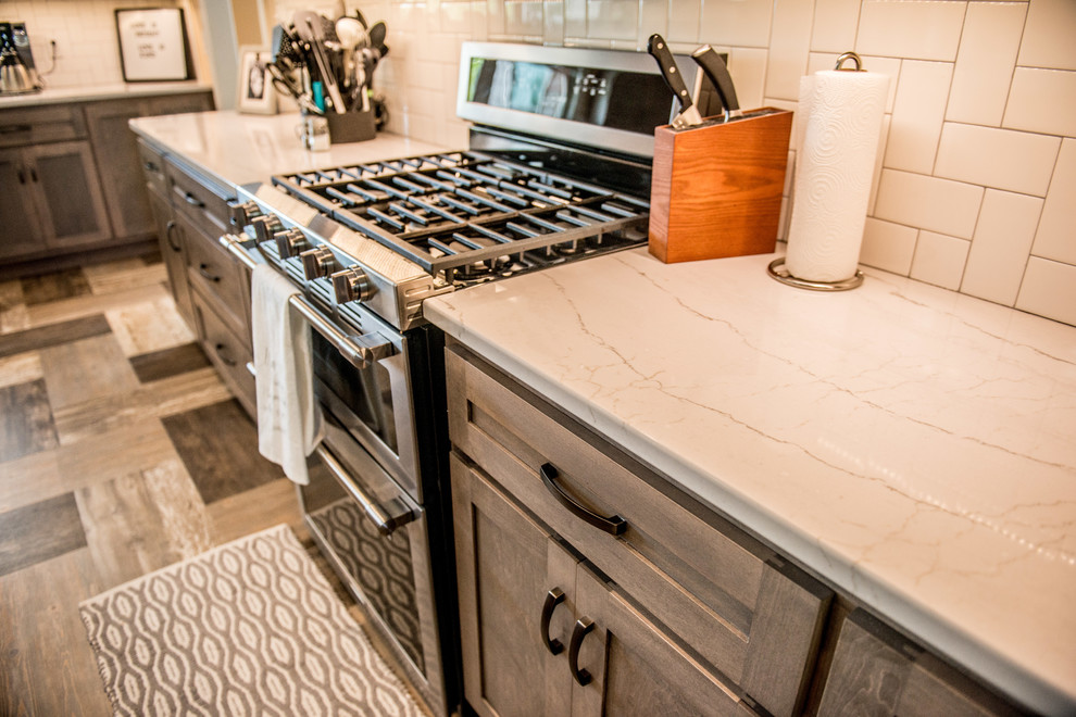 Open concept kitchen - large transitional l-shaped vinyl floor and multicolored floor open concept kitchen idea with a farmhouse sink, shaker cabinets, gray cabinets, quartz countertops, white backsplash, subway tile backsplash, stainless steel appliances, an island and white countertops