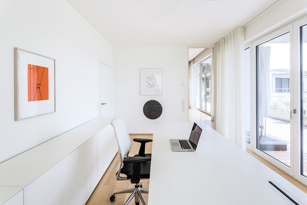 This is an example of a mid-sized modern study room in Cologne with white walls, light hardwood floors, no fireplace, a freestanding desk and beige floor.