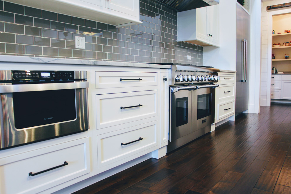 Transitional single-wall dark wood floor open concept kitchen photo in Chicago with a farmhouse sink, beaded inset cabinets, white cabinets, quartzite countertops, gray backsplash, ceramic backsplash, stainless steel appliances and an island