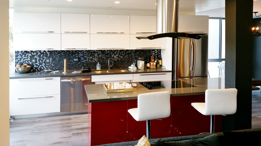 This is an example of a large modern single-wall eat-in kitchen in Los Angeles with a single-bowl sink, flat-panel cabinets, white cabinets, black splashback, mosaic tile splashback, stainless steel appliances, light hardwood floors and with island.