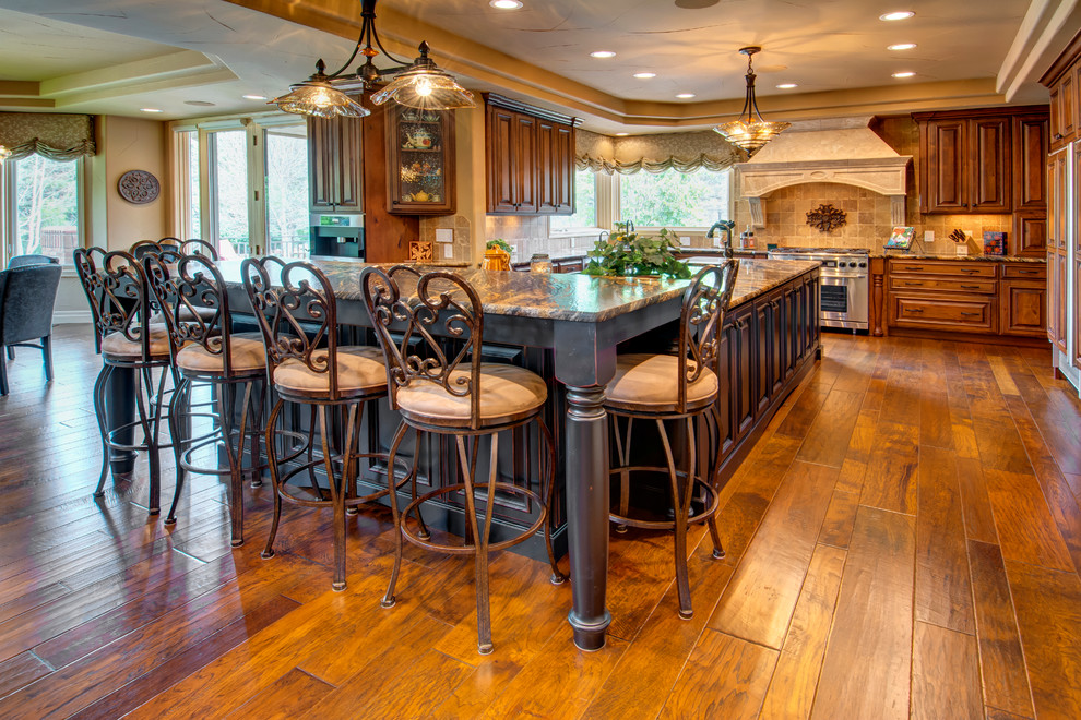 Large traditional l-shaped eat-in kitchen in Denver with medium hardwood floors, with island, a single-bowl sink, recessed-panel cabinets, medium wood cabinets, granite benchtops, beige splashback, stone tile splashback and stainless steel appliances.