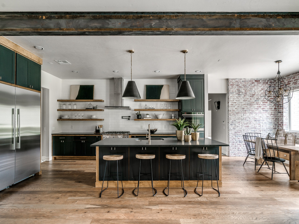 Design ideas for a country l-shaped eat-in kitchen in Oklahoma City with an undermount sink, shaker cabinets, green cabinets, white splashback, subway tile splashback, stainless steel appliances, medium hardwood floors, with island, brown floor and black benchtop.