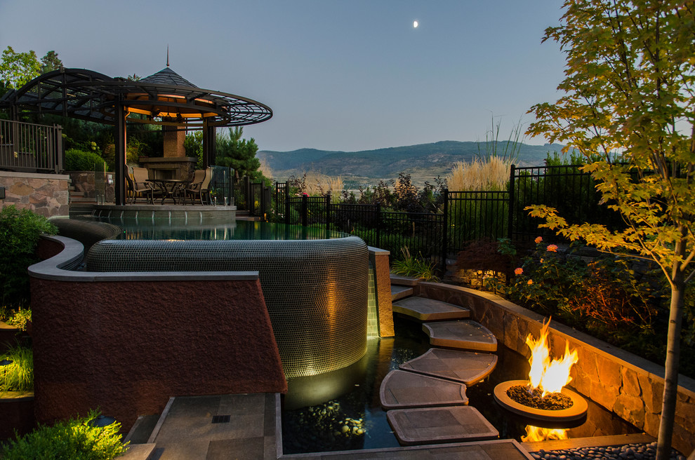 Photo of a mid-sized eclectic backyard custom-shaped infinity pool in Vancouver with natural stone pavers.