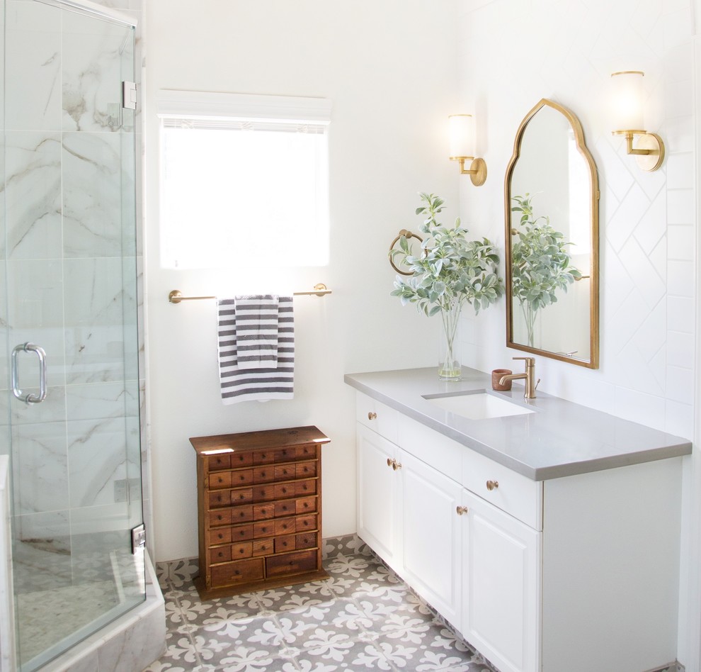 Photo of a mid-sized transitional 3/4 bathroom in Other with raised-panel cabinets, white cabinets, a freestanding tub, an alcove shower, a two-piece toilet, white tile, porcelain tile, white walls, porcelain floors, an undermount sink, solid surface benchtops, grey floor and a hinged shower door.