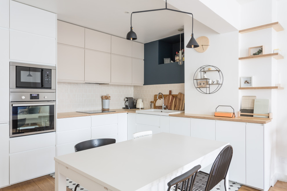 Design ideas for a mid-sized scandinavian l-shaped open plan kitchen in London with a drop-in sink, white cabinets, wood benchtops, beige splashback, terra-cotta splashback, stainless steel appliances, cement tiles, multi-coloured floor, beige benchtop, flat-panel cabinets and no island.