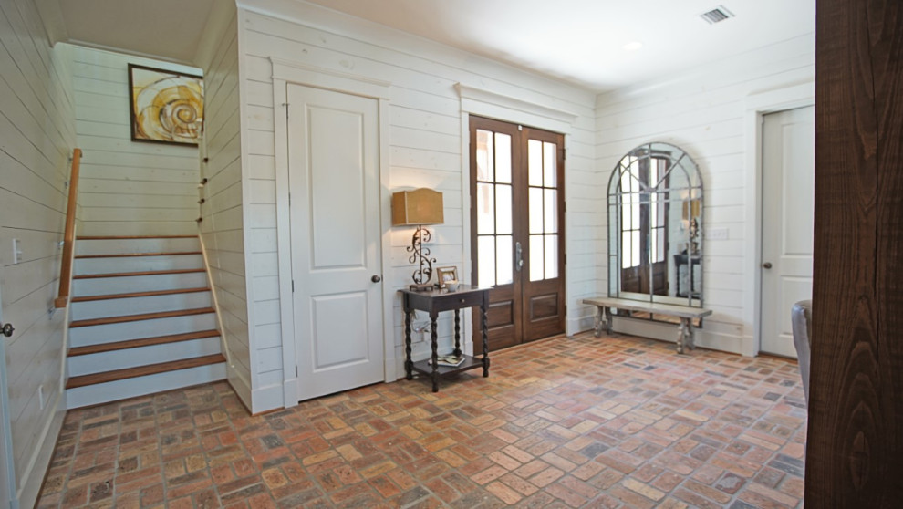 This is an example of a country foyer in Other with white walls, brick floors, a double front door, a brown front door and multi-coloured floor.