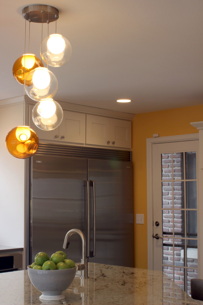 Large transitional l-shaped light wood floor eat-in kitchen photo with a farmhouse sink, shaker cabinets, white cabinets, glass countertops, white backsplash, subway tile backsplash, stainless steel appliances and an island