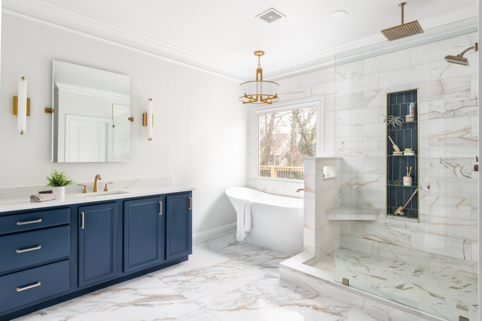 Design ideas for a mid-sized transitional master bathroom in Atlanta with recessed-panel cabinets, blue cabinets, a freestanding tub, a corner shower, a two-piece toilet, white tile, marble, white walls, porcelain floors, an undermount sink, engineered quartz benchtops, white floor, an open shower, white benchtops, a niche, a double vanity and a built-in vanity.