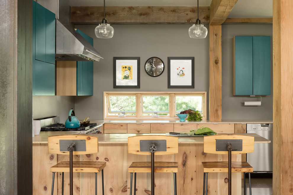 Photo of a country u-shaped open plan kitchen in Portland Maine with flat-panel cabinets, turquoise cabinets, stainless steel appliances, a peninsula and beige benchtop.