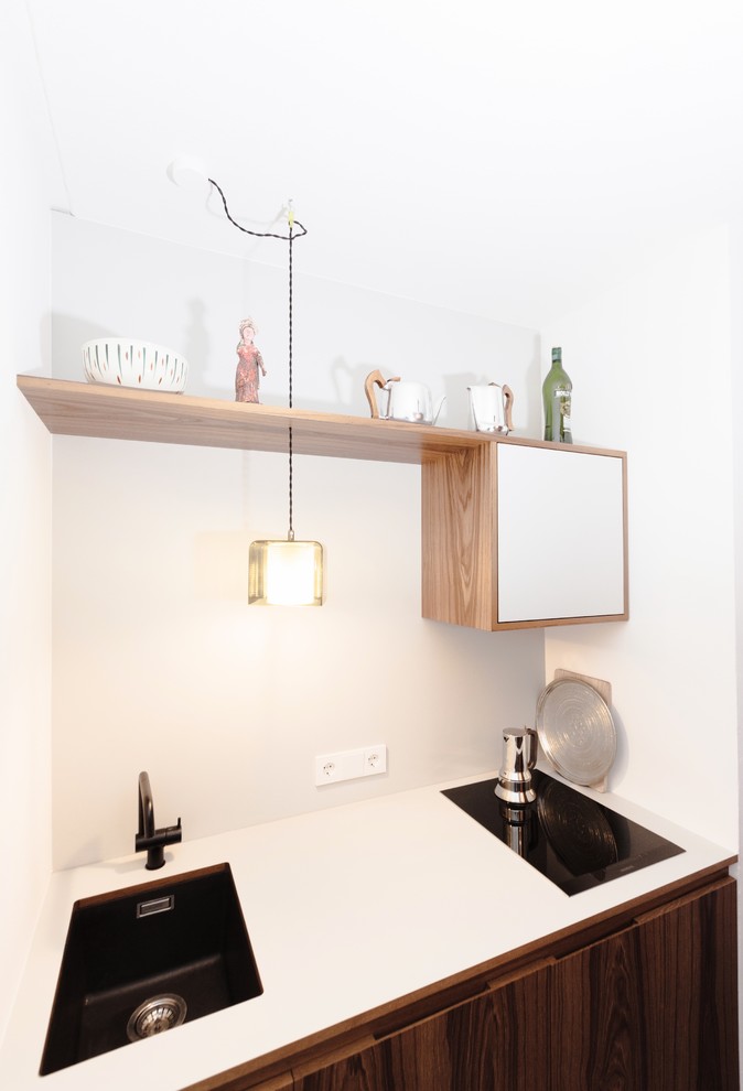 Inspiration for a small midcentury single-wall separate kitchen in Munich with an undermount sink, flat-panel cabinets, dark wood cabinets, solid surface benchtops, grey splashback, black appliances, concrete floors and black floor.