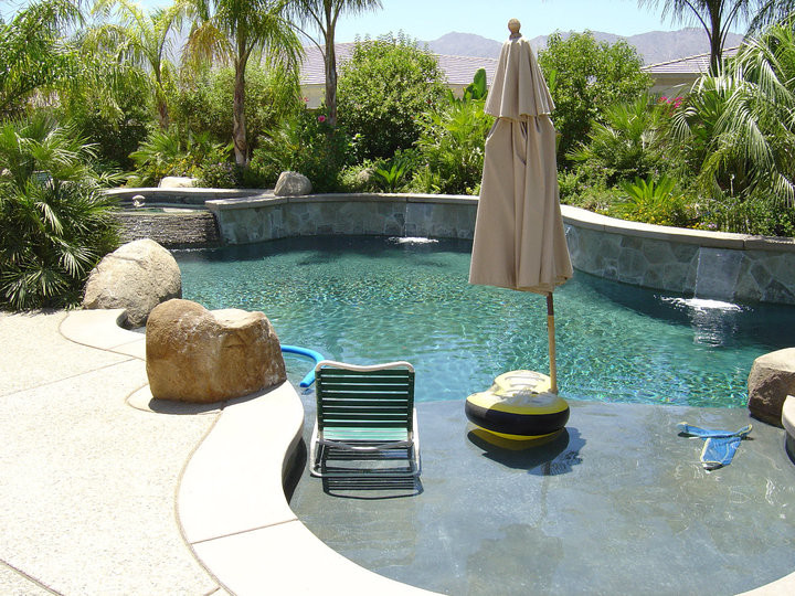 This is an example of a mid-sized tropical backyard custom-shaped natural pool in Orange County with concrete pavers and a hot tub.