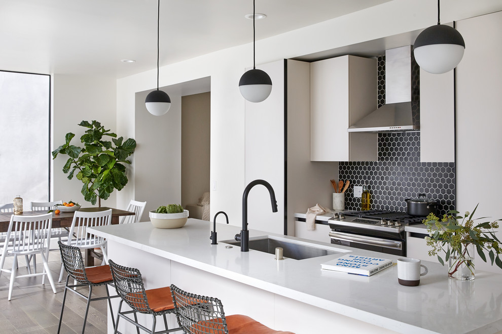Photo of a mid-sized contemporary eat-in kitchen in Los Angeles with an undermount sink, flat-panel cabinets, quartz benchtops, black splashback, porcelain splashback, stainless steel appliances, light hardwood floors, with island, white benchtop and beige floor.
