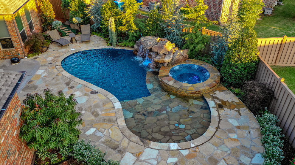 Foto de piscina natural clásica renovada de tamaño medio a medida en patio trasero con paisajismo de piscina y adoquines de piedra natural