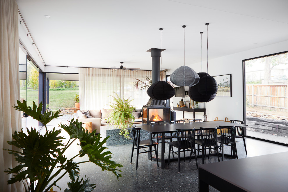 Large contemporary dining room in Other with white walls, concrete floors, a two-sided fireplace, a concrete fireplace surround and black floor.