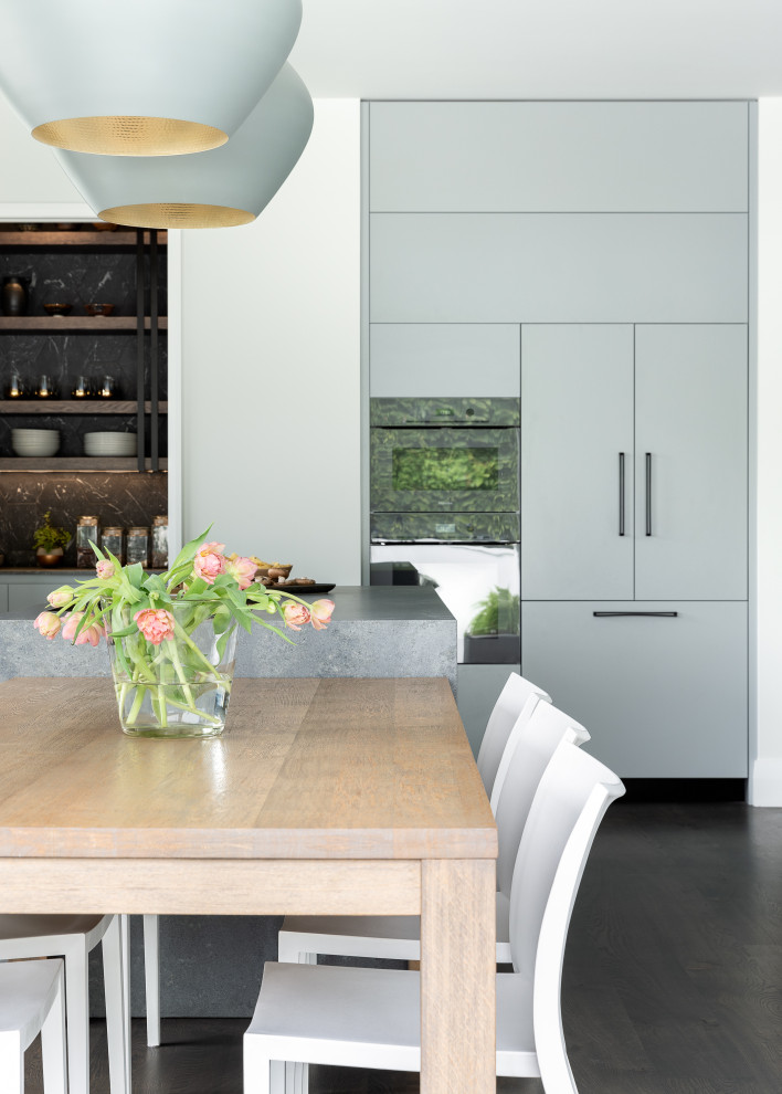 Bild på ett mellanstort funkis grå grått kök, med en enkel diskho, släta luckor, grå skåp, bänkskiva i kvarts, svart stänkskydd, stänkskydd i porslinskakel, mörkt trägolv, en köksö och brunt golv