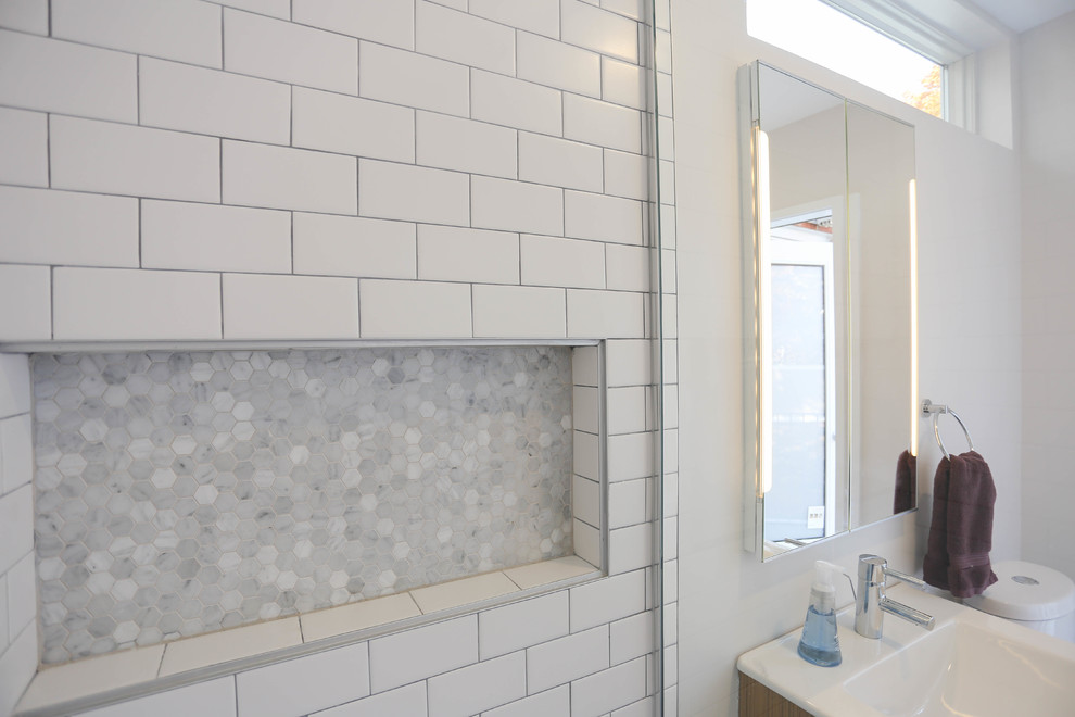 Photo of a small modern master bathroom in Baltimore with flat-panel cabinets, medium wood cabinets, a corner shower, a one-piece toilet, white tile, subway tile, white walls, porcelain floors, a wall-mount sink and engineered quartz benchtops.