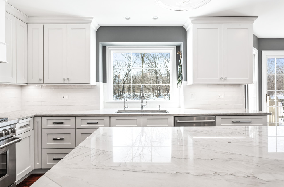 Inspiration for a large transitional u-shaped medium tone wood floor and brown floor eat-in kitchen remodel in Chicago with a single-bowl sink, shaker cabinets, white cabinets, quartzite countertops, white backsplash, porcelain backsplash, stainless steel appliances, an island and gray countertops