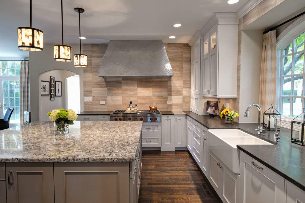 Kitchen - transitional l-shaped kitchen idea in Chicago with a farmhouse sink, beige backsplash, stone tile backsplash and stainless steel appliances