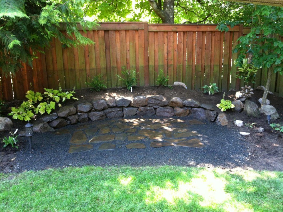 This is an example of a mid-sized traditional backyard full sun garden in Portland with a retaining wall and natural stone pavers.