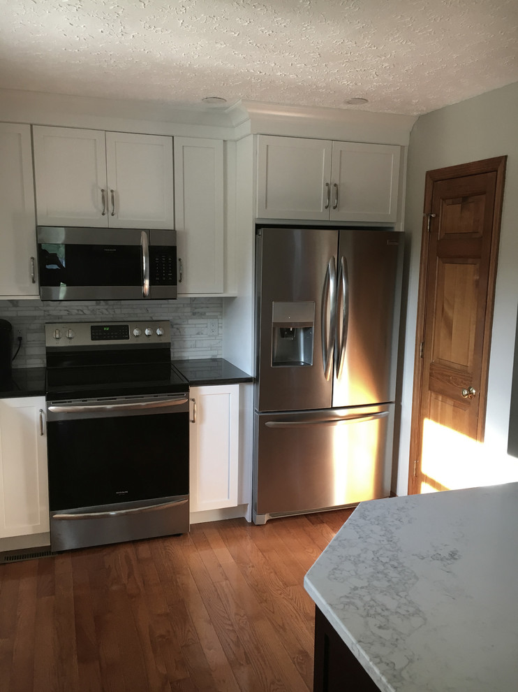 Inspiration for a large transitional single-wall medium tone wood floor eat-in kitchen remodel with an undermount sink, shaker cabinets, white cabinets, granite countertops, multicolored backsplash, marble backsplash, stainless steel appliances, an island and black countertops