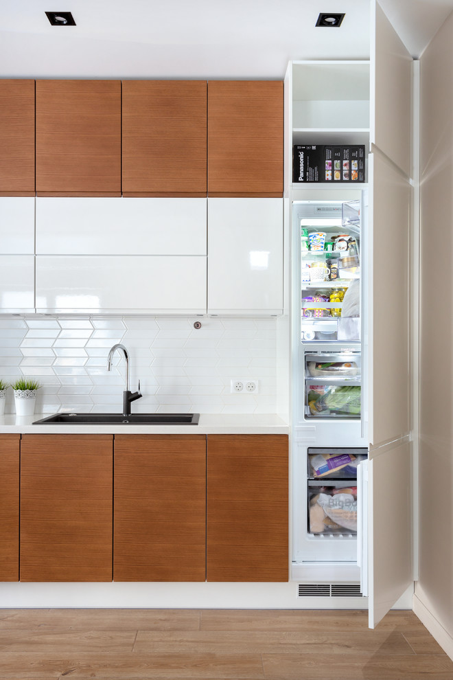 Photo of a mid-sized scandinavian single-wall eat-in kitchen in Moscow with a drop-in sink, flat-panel cabinets, white cabinets, solid surface benchtops, white splashback, ceramic splashback, black appliances, medium hardwood floors, no island, brown floor and white benchtop.