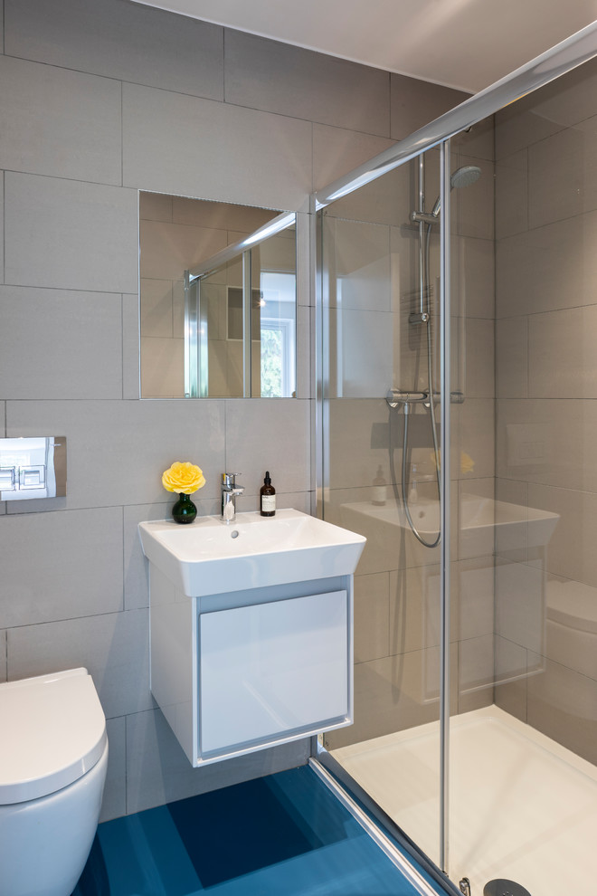 Inspiration for a contemporary bathroom in London with flat-panel cabinets, white cabinets, an alcove shower, a wall-mount toilet, gray tile, grey walls, a console sink, blue floor and a hinged shower door.