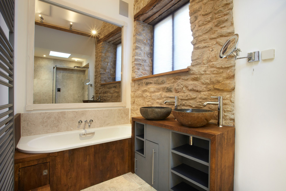Small traditional 3/4 bathroom in Wiltshire with a drop-in sink, open cabinets, grey cabinets, wood benchtops, an alcove tub, a corner shower, a one-piece toilet, beige tile, stone tile, white walls and porcelain floors.