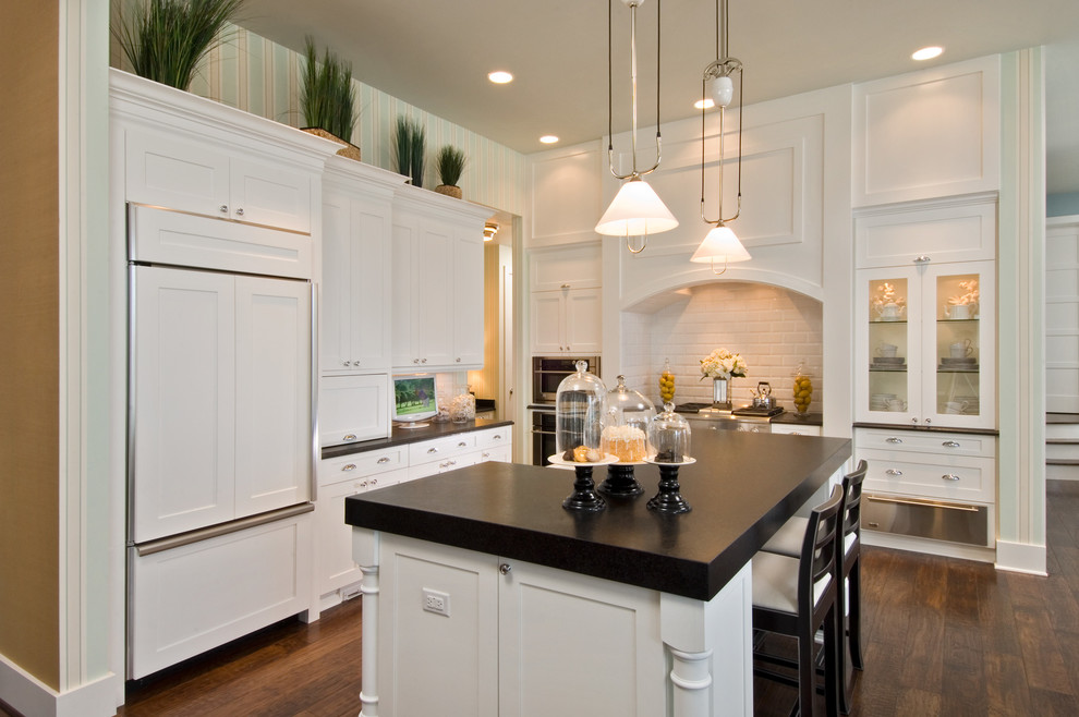 Photo of a large traditional l-shaped eat-in kitchen in Miami with subway tile splashback, a farmhouse sink, shaker cabinets, white cabinets, white splashback, panelled appliances, dark hardwood floors and with island.