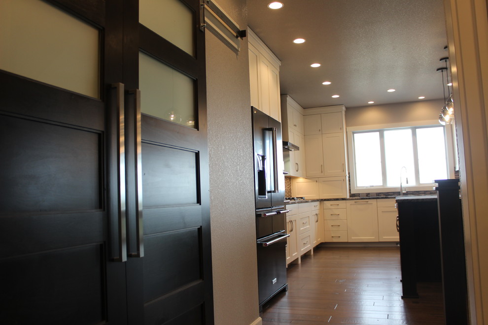 Inspiration for a large transitional l-shaped medium tone wood floor and brown floor kitchen remodel with an undermount sink, shaker cabinets, white cabinets, granite countertops, multicolored backsplash, mosaic tile backsplash, black appliances and an island